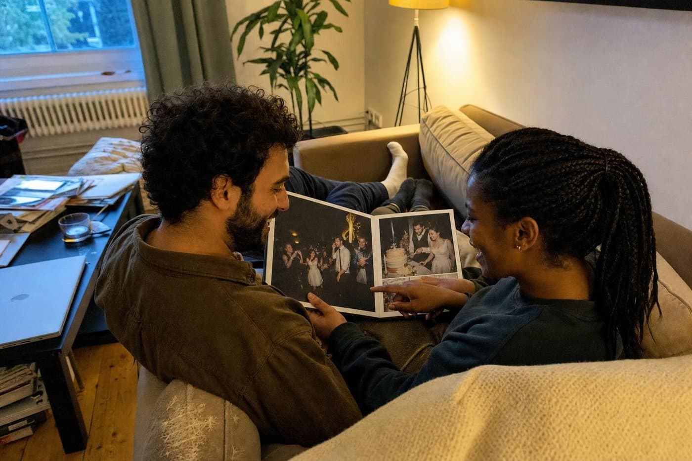 Paar zeigt sich abends auf dem Sofa gegenseitig Bilder im aufgeschlagenen Fotobuch