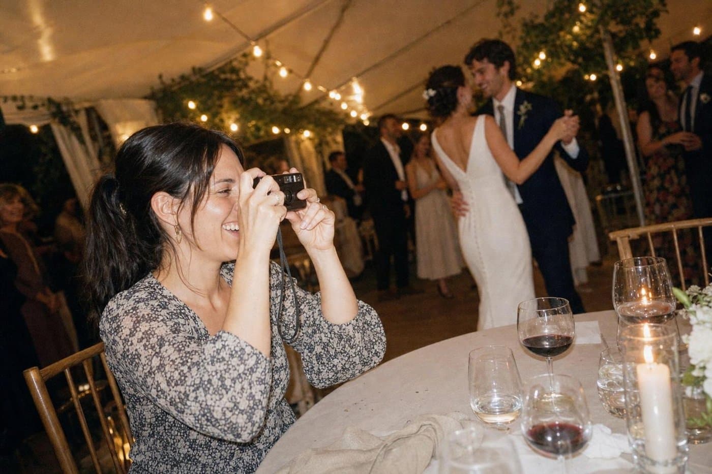 Gästin sitzt am gedeckten Tisch und fotografiert das tanzende Brautpaar im Festzelt